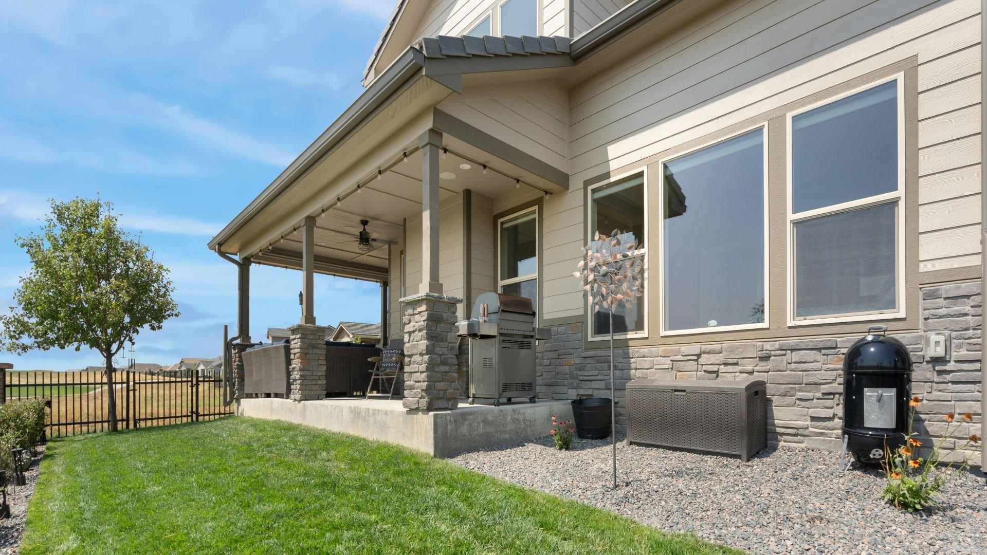 Modern home with covered patio, grill, and manicured lawn on sunny day