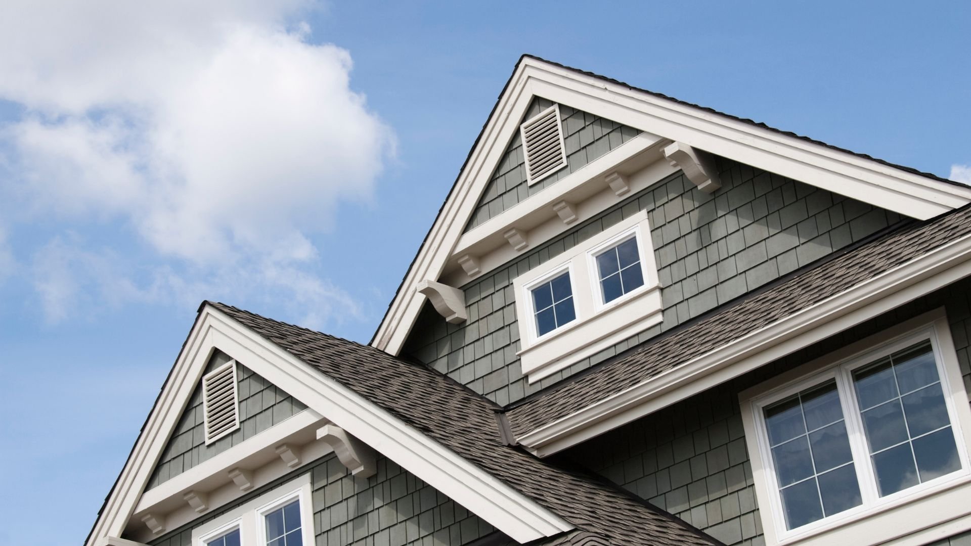 Gray shingled house with white trim and multiple windows under blue sky