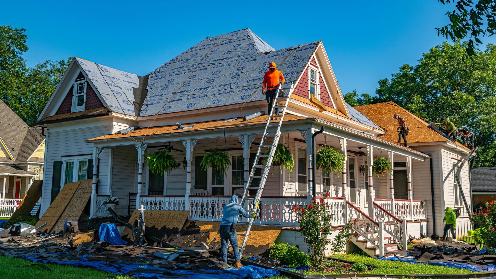 Workers replacing roof on a white Victorian-style house with blue sky