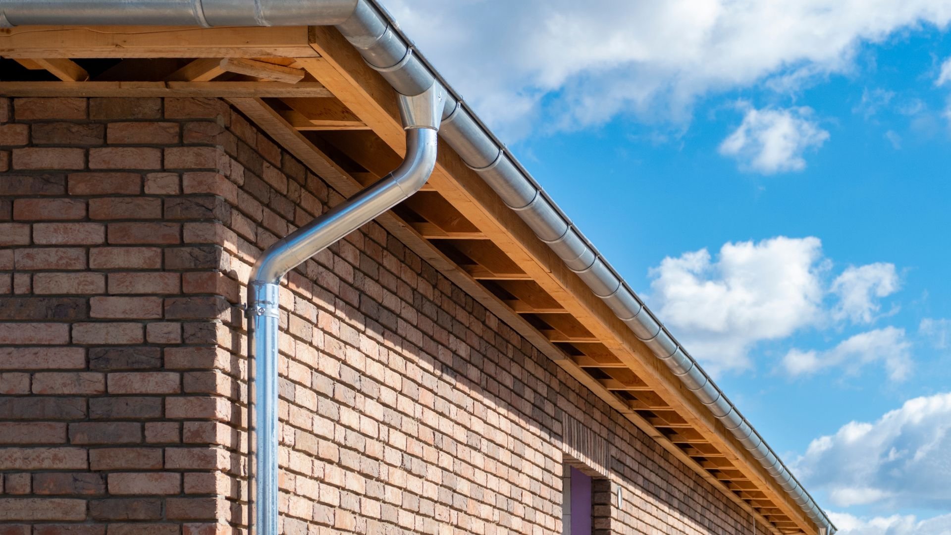 Brick building with metal gutters and wooden roof against blue sky