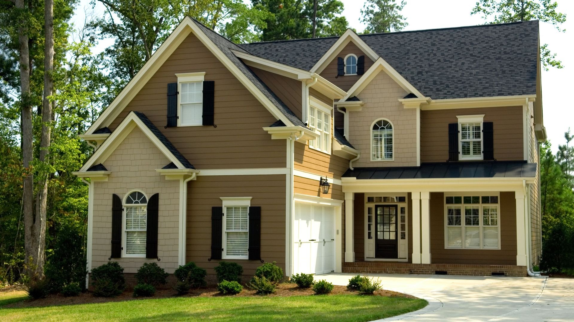 Two-story brown house with black shutters and white trim surrounded by trees